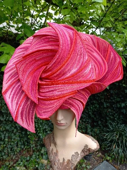 Roze hoedobject met draaiende, geribbelde vormen op een houten sculptuur in het groen